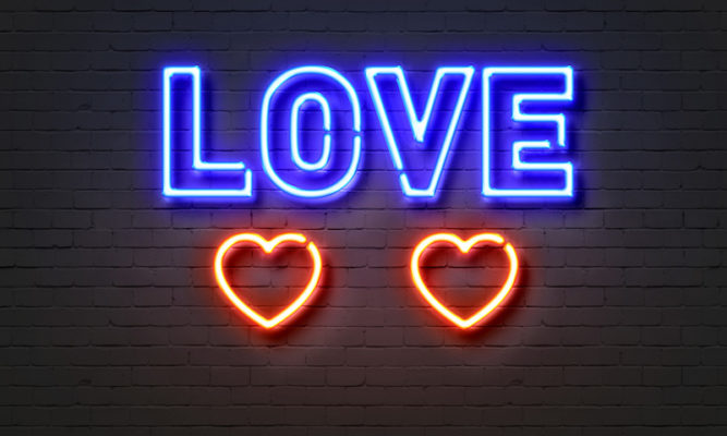 love and two red hearts in neon letters on brick wall