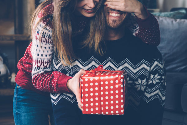 woman covering mans eyes giving him a christmas gift