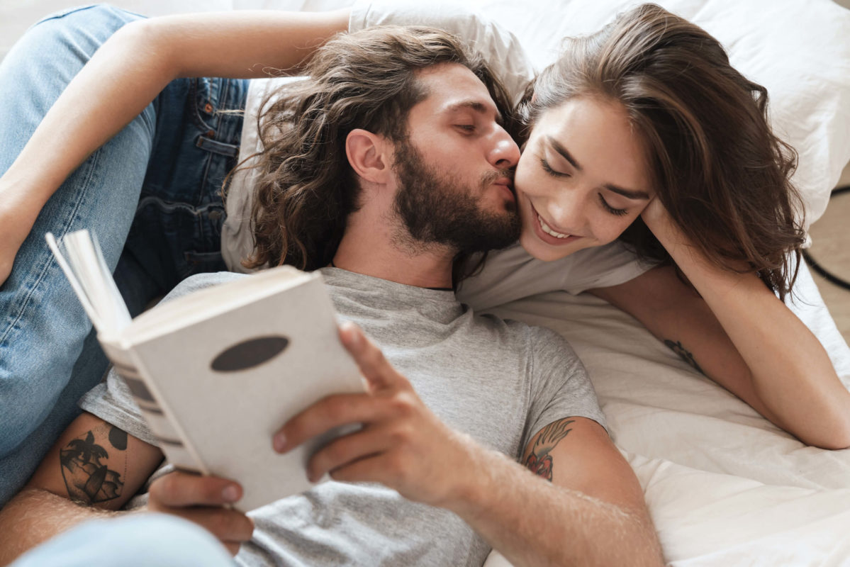 couple laying on bed cuddling with a book