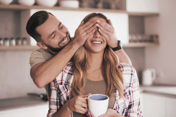 man cover womans eyes while she holds cup of coffee