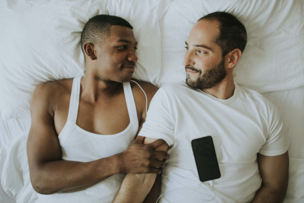 two men laying in bed listening to music