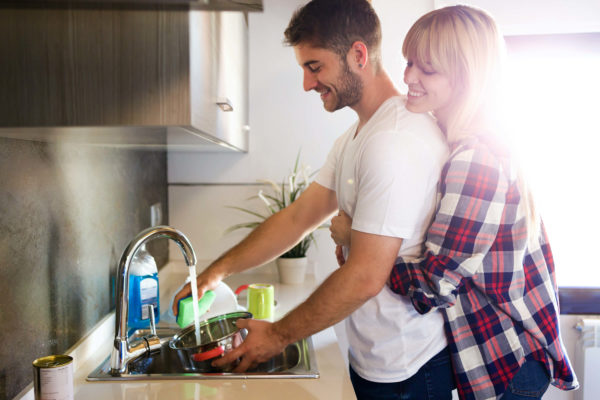 woman hugging man from behind while he does the dishes